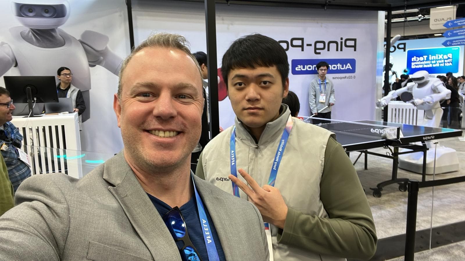 Justin networking on the CES show floor with ping-pong robots in the background